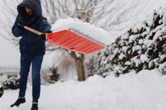 man in blue jacket and jeans removing snow with red shovel